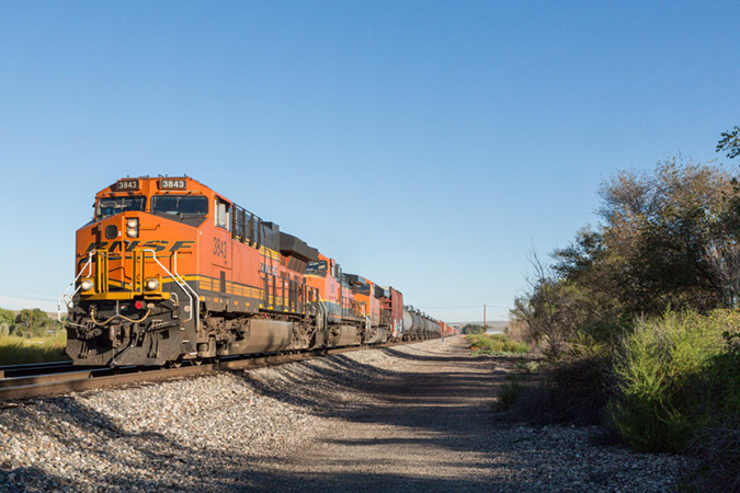 BNSF 3843, also a Tier 4 GE ET44C4, leads a mixed freight train toward a grade crossing.